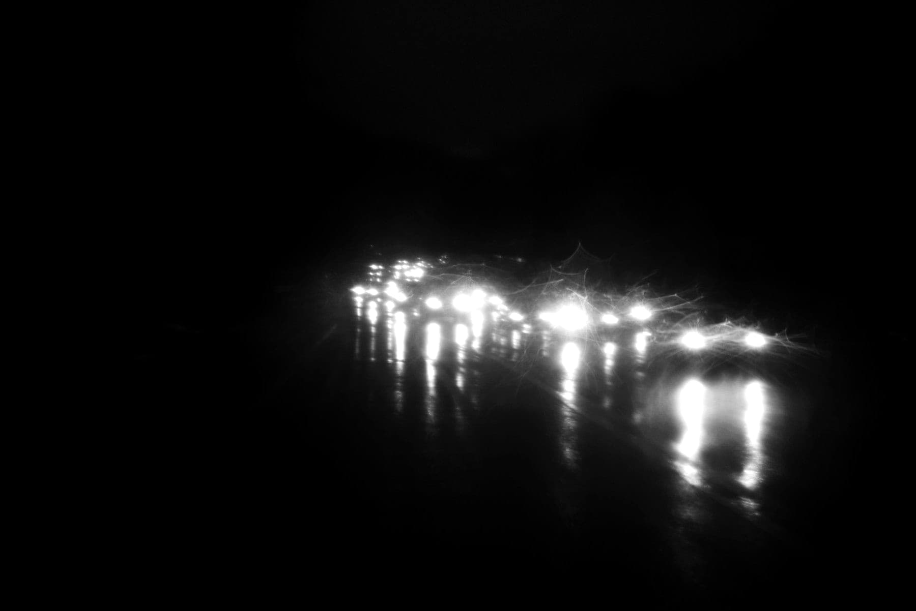 Blurred headlights reflected on a wet road at night.