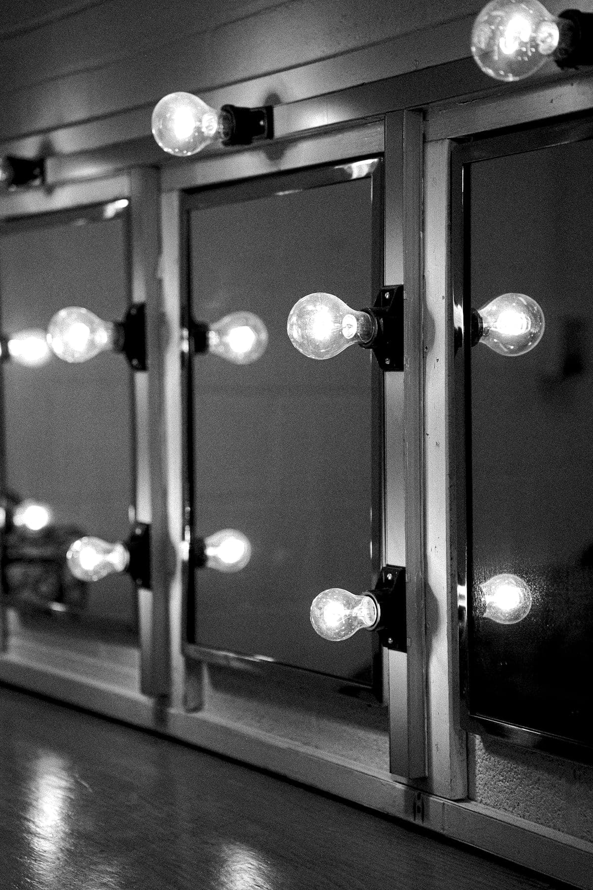 Dressing-room mirrors framed by bare bulbs, reflections repeating in the glass.