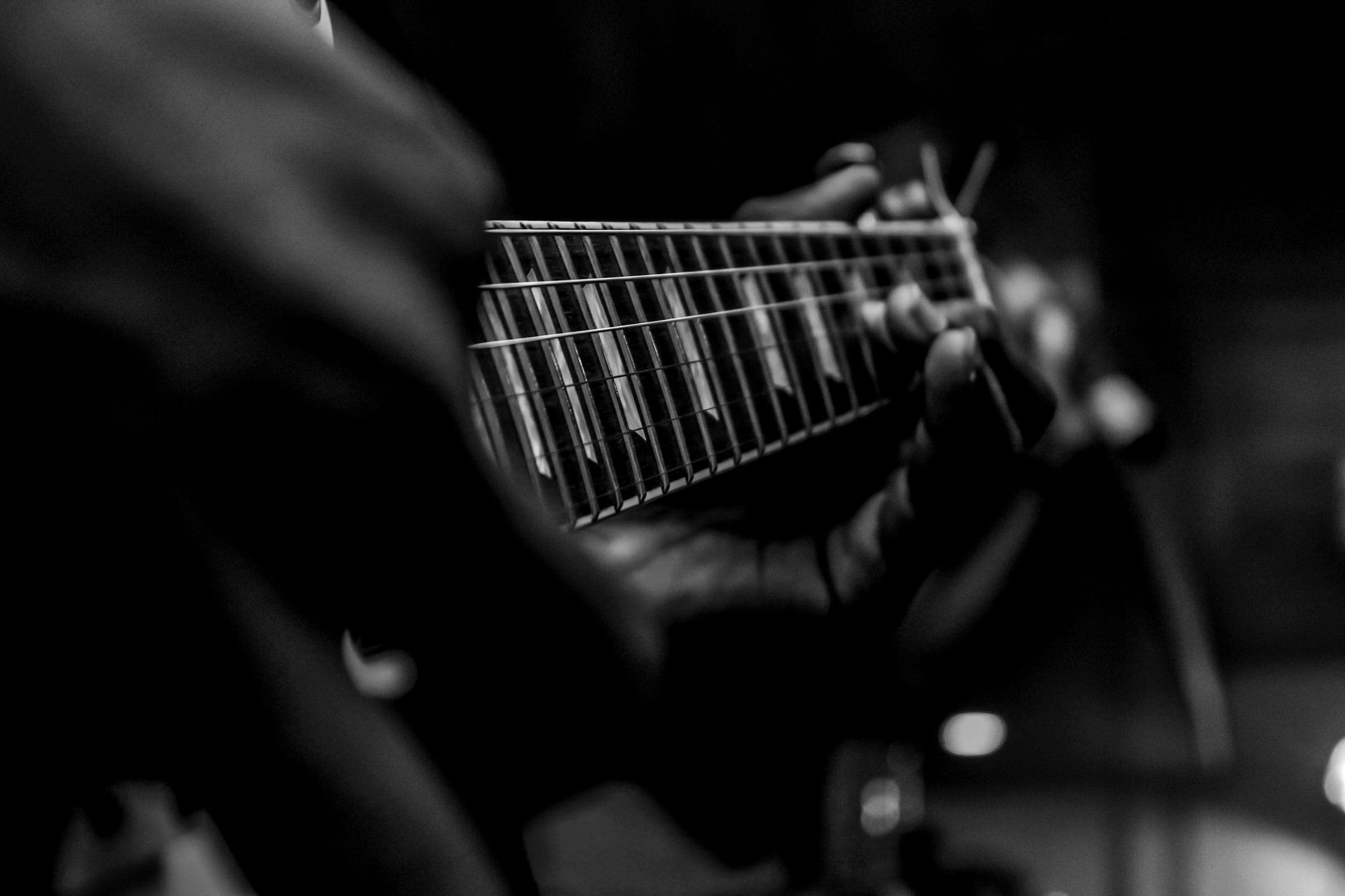 Over-the-shoulder view of a hand fretting an electric guitar in low light.