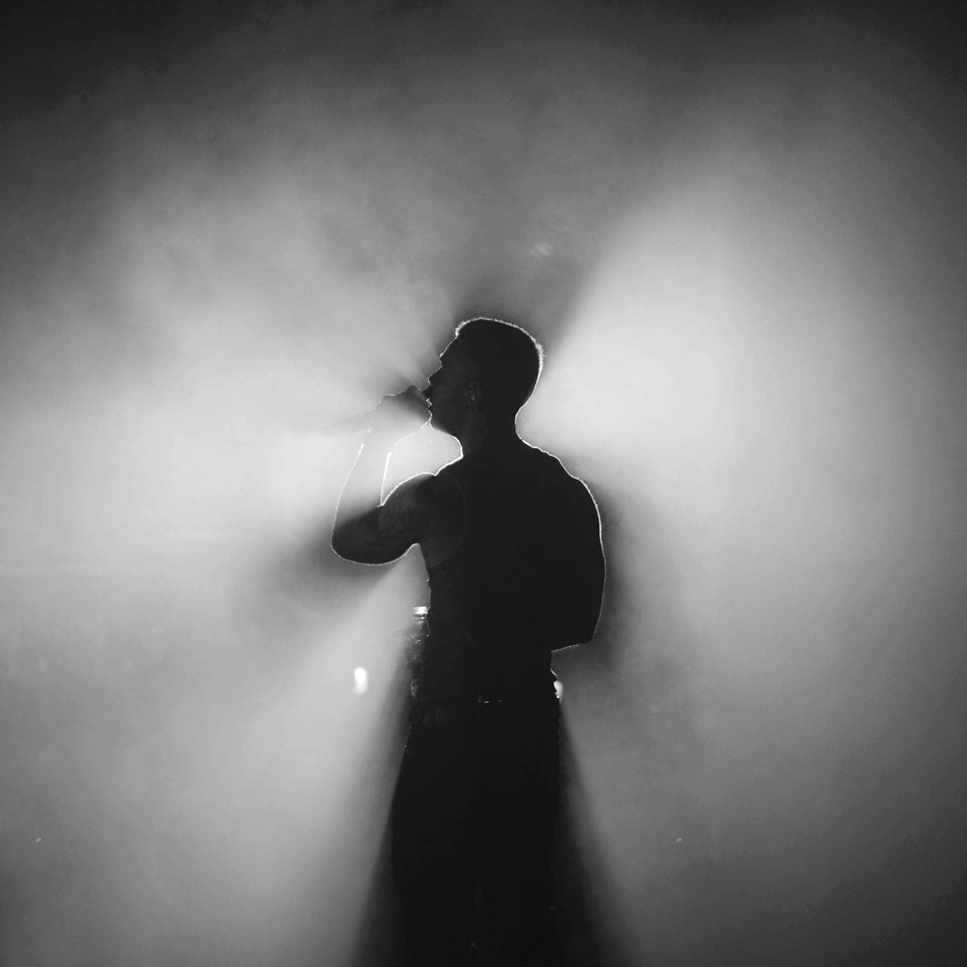 Glass Hours artwork: a singer seen from behind in silhouette, backlight fanning out through thick stage haze.